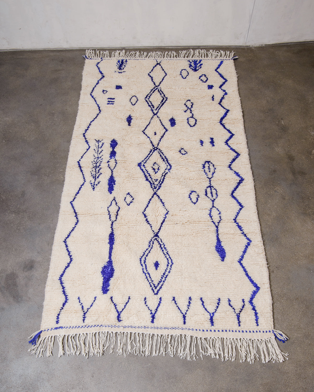 Berberlin Azilal rug made of fluffy cream wool and bright blue cotton, laying flat on cement floor.